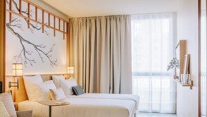 Habitación de hotel con cama, mesitas de noche, lámpara de pared, un amplio ventanal con cortinas y un elemento decorativo en la pared.