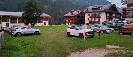 Un área de estacionamiento con varios coches, un cartel que indica un hotel y edificios con arquitectura tradicional al fondo.