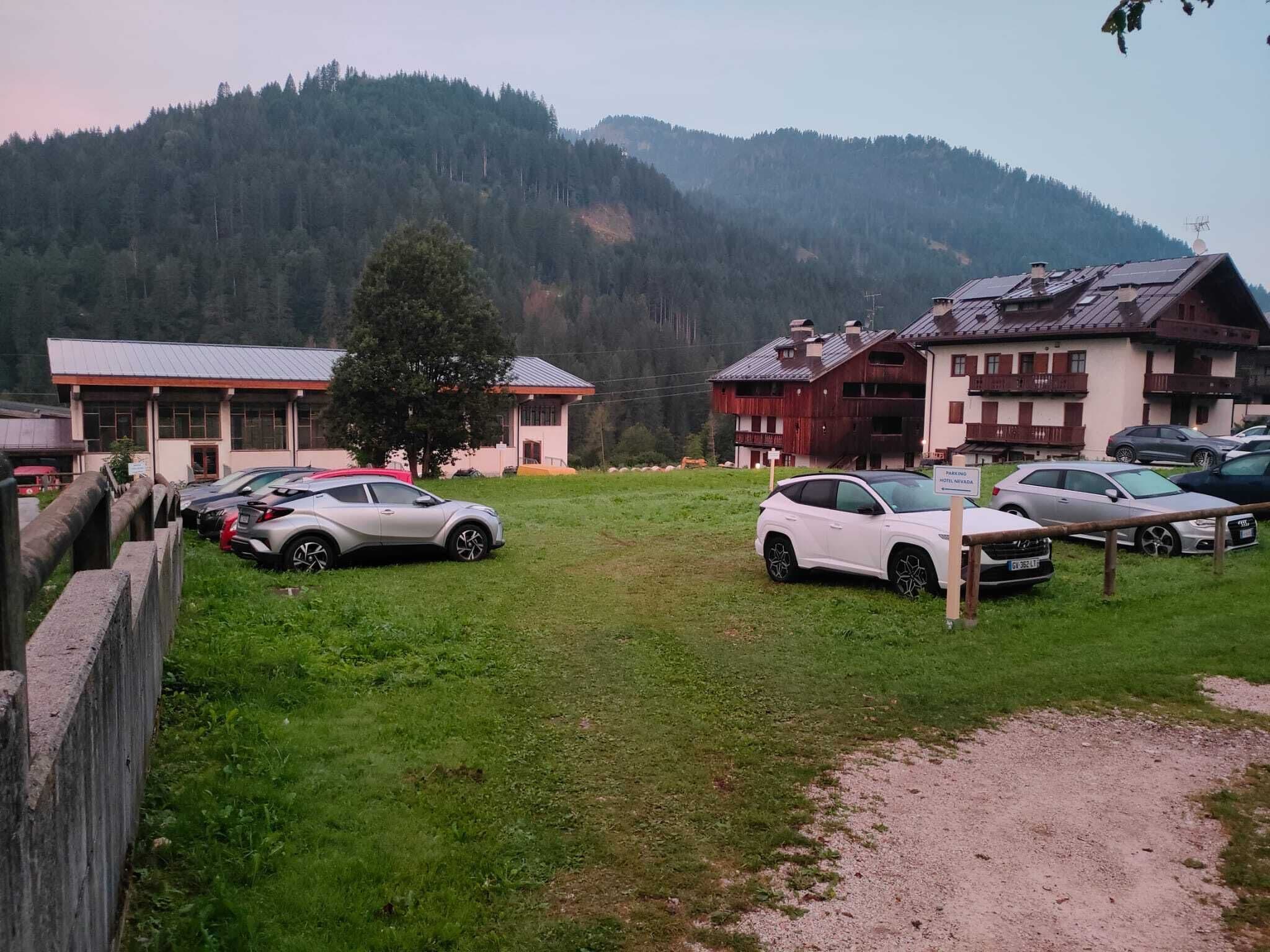 A parking area with several cars, a building with a red roof, and a mountainous backdrop.