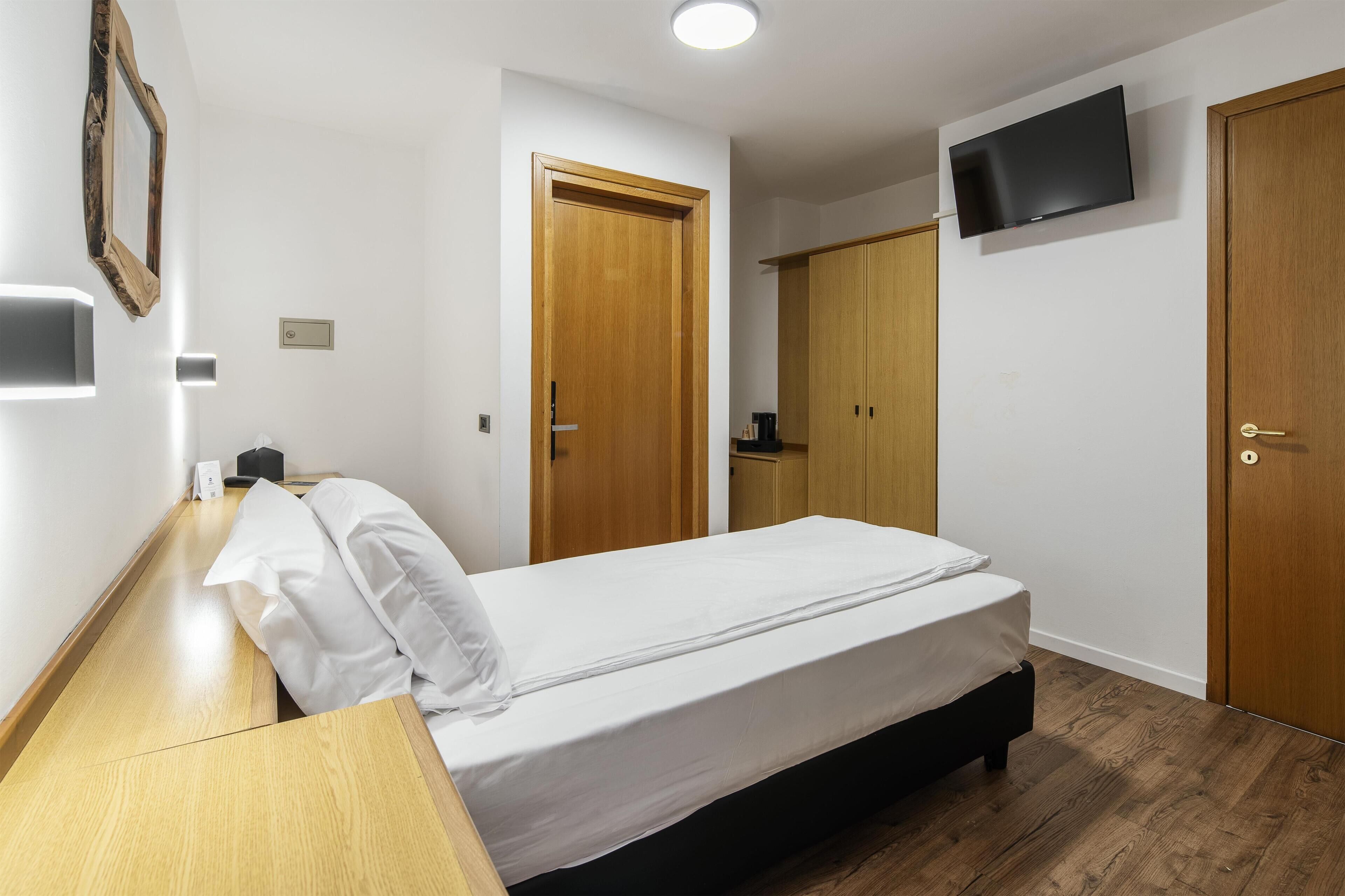 Camera d'albergo con un letto, una scrivania, un armadio e una TV a parete.