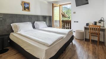 Ein Schlafzimmer mit Bett, Nachttischen, einem Schreibtisch mit Stuhl, einem Fernseher und einem Fenster mit Blick auf einen Wald.