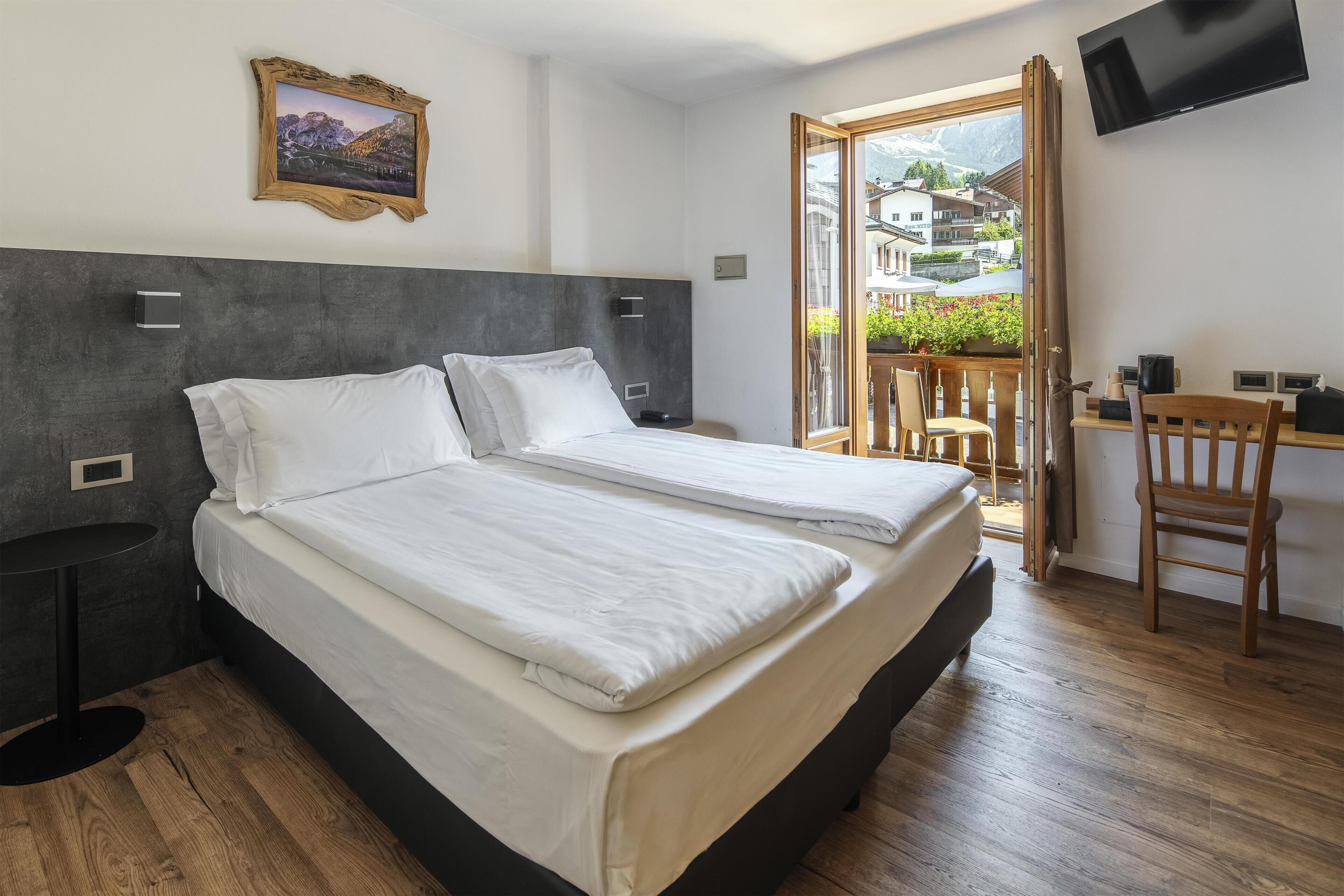 A hotel room with a bed, a desk, a chair, a TV, and a window with a view of buildings.