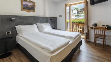 Habitación de hotel con cama, escritorio, silla, televisor y ventana con vistas a edificios.