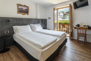 Habitación de hotel con cama, escritorio, silla, televisor y ventana con vistas a edificios.