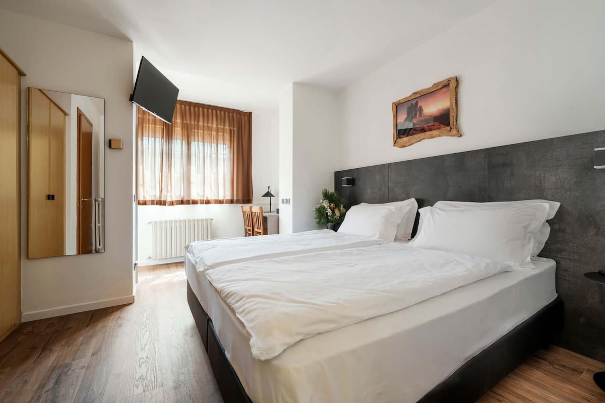 Ein Schlafzimmer mit einem großen Bett, einem flachbildfernseher an der Wand, einem Fenster mit Vorhängen und einem gerahmten Bild über dem Bett.