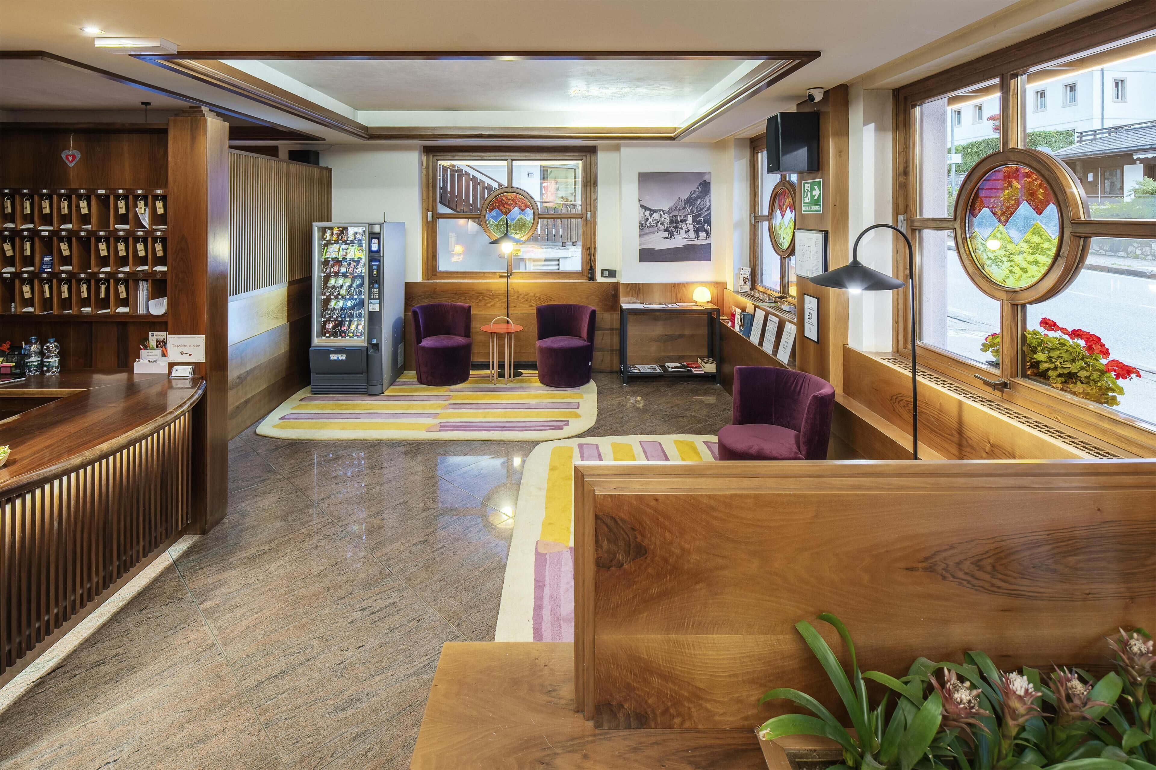 Eine Hotelhalle mit Rezeption, Verkaufsautomaten, Sitzgelegenheiten und großen Fenstern.