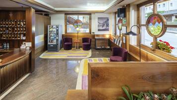 Eine Hotelhalle mit Rezeption, Verkaufsautomaten, Sitzgelegenheiten und großen Fenstern.