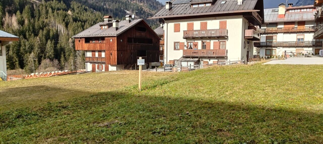Un bâtiment doté d’une façade en bois et de balcons, entouré d’une zone verdoyante et avec des montagnes en arrière-plan.