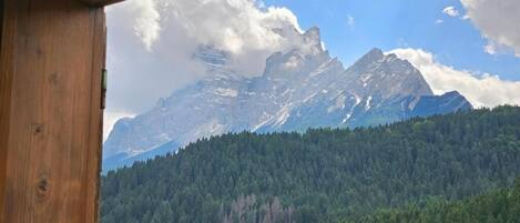 A mountain view from a wooden cabin with a forested hillside.