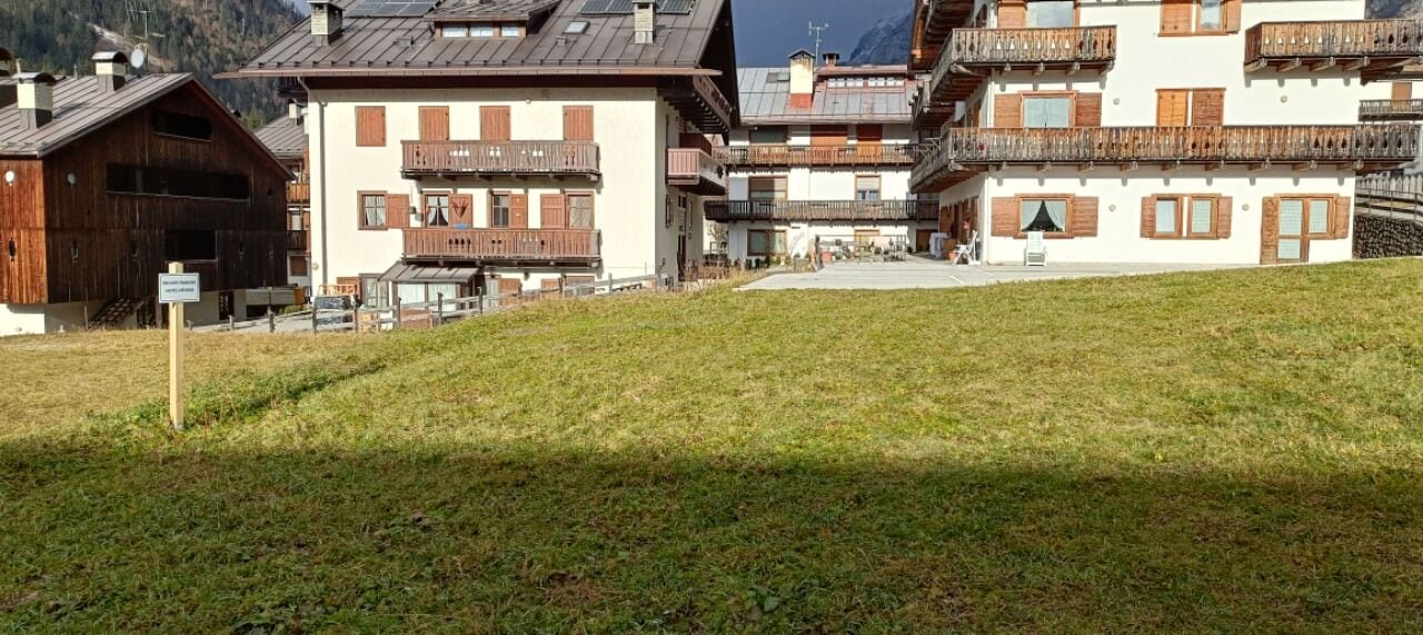 A row of traditional chalet-style buildings with wooden balconies, a grassy foreground, and a mountainous backdrop.
