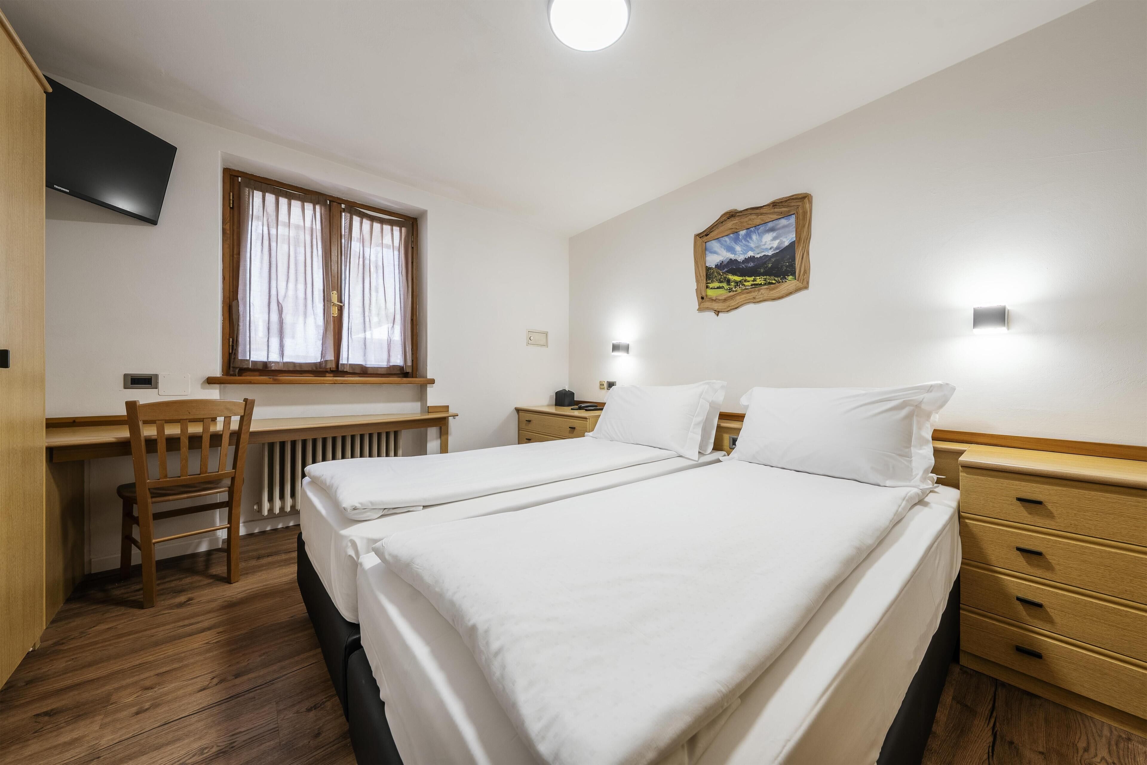 Ein Hotelzimmer mit Bett, Schreibtisch, Stuhl, Heizkörper, Fernseher und einem Bild an der Wand.