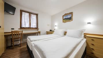 Een hotelkamer met een bed, bureau, stoel, radiator, televisie en een schilderij aan de muur.
