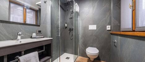 A modern bathroom with a glass-enclosed shower, a white sink, and a toilet.