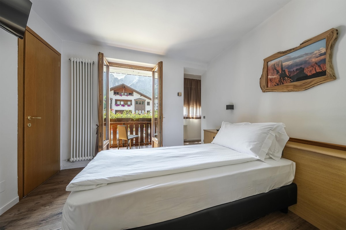 Una habitación de hotel con una cama, cabecera de madera, ventana con vistas a la montaña y un cuadro en la pared.