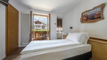 Une chambre d’hôtel avec un lit, une tête de lit en bois, une fenêtre donnant sur une montagne et un tableau accroché au mur.