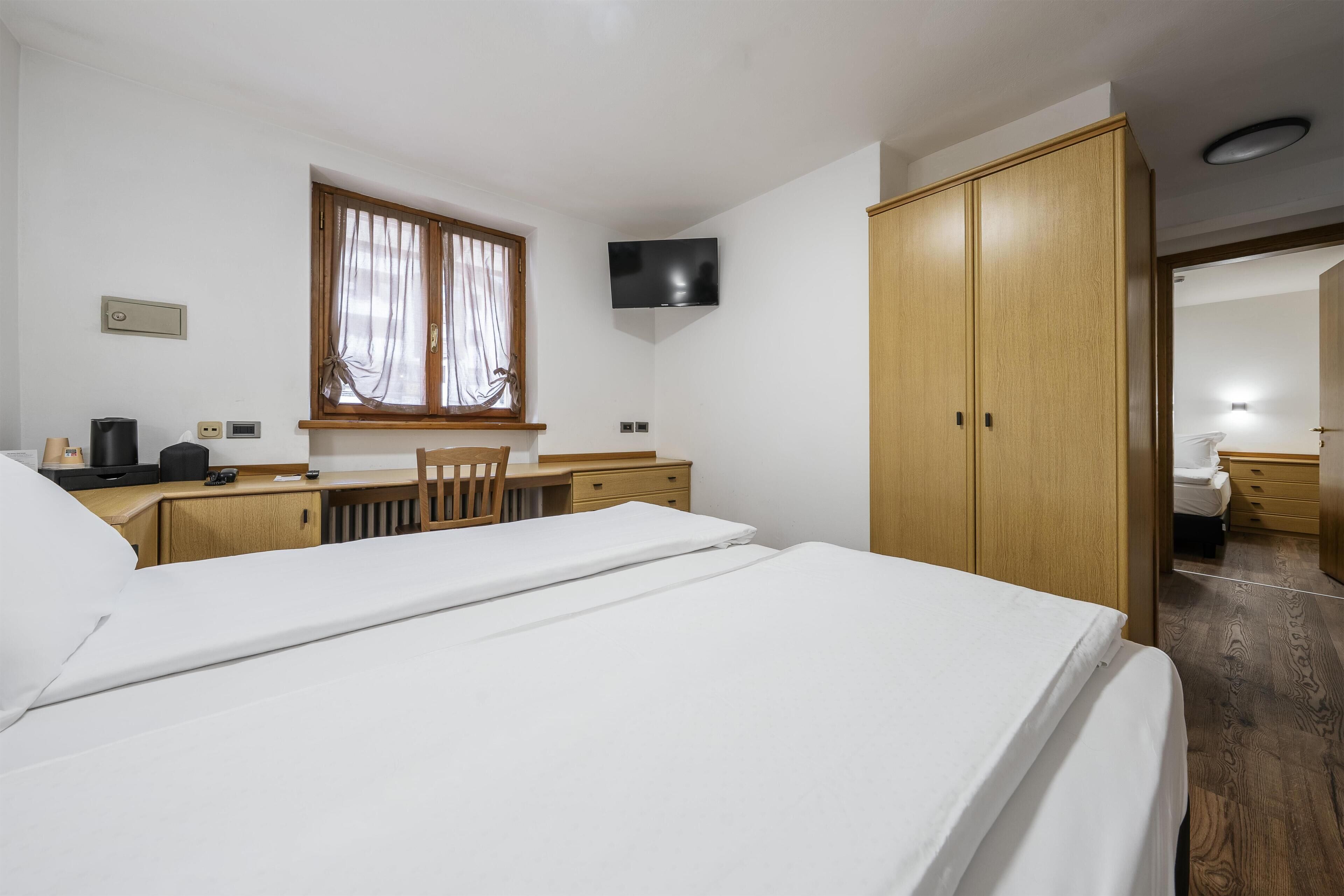 A hotel room with a bed, a desk, a chair, a wardrobe, and a television.