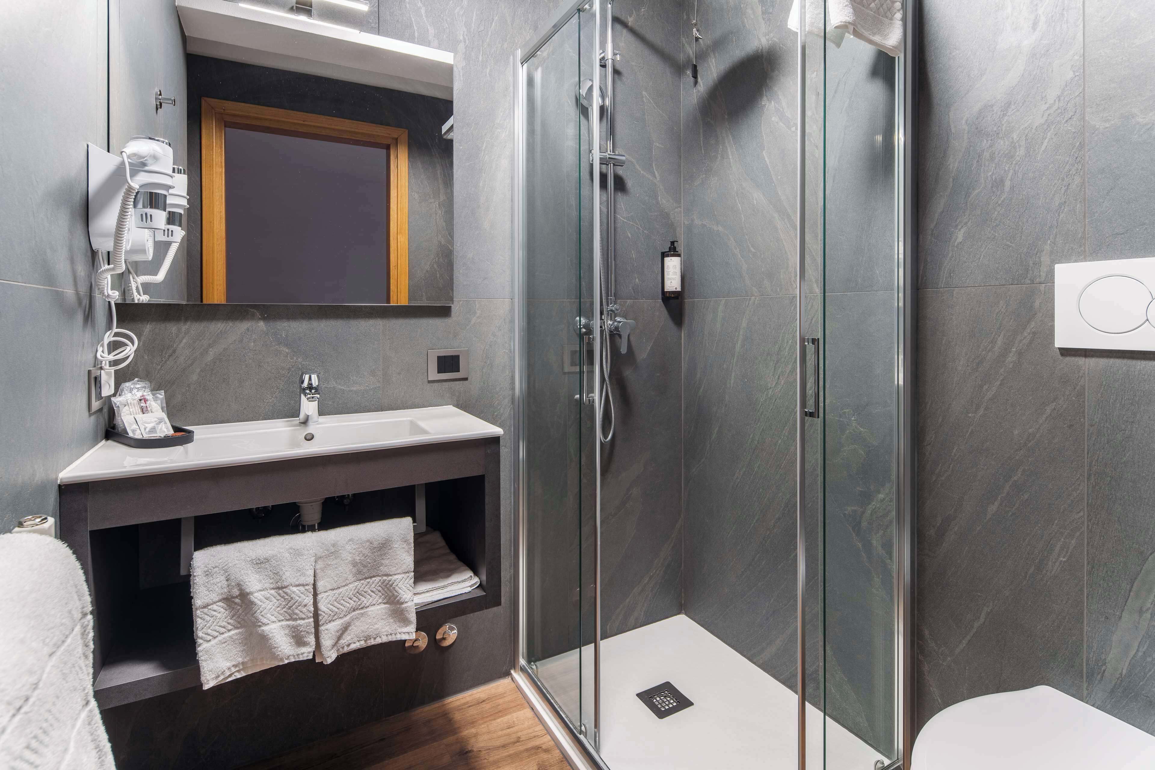 Un baño moderno con ducha de vidrio, un lavabo con toallero y un espejo con marco de madera.