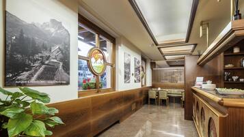 A hotel corridor with wooden paneling, a dining area with patterned chairs, and artwork on the walls.