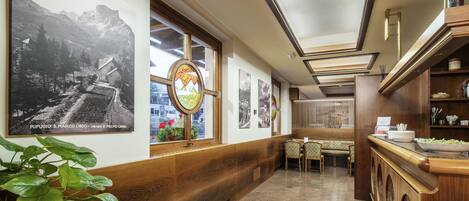 A hotel corridor with wooden paneling, a dining area with patterned chairs, and artwork on the walls.