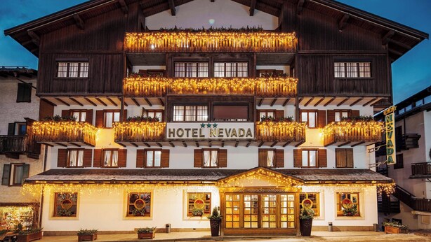 A multi-story hotel with a traditional Alpine architectural style, featuring balconies with string lights and a prominent sign reading "HOTEL NEVADA". - Best Western Hotel Nevada (San Vito di Cadore)