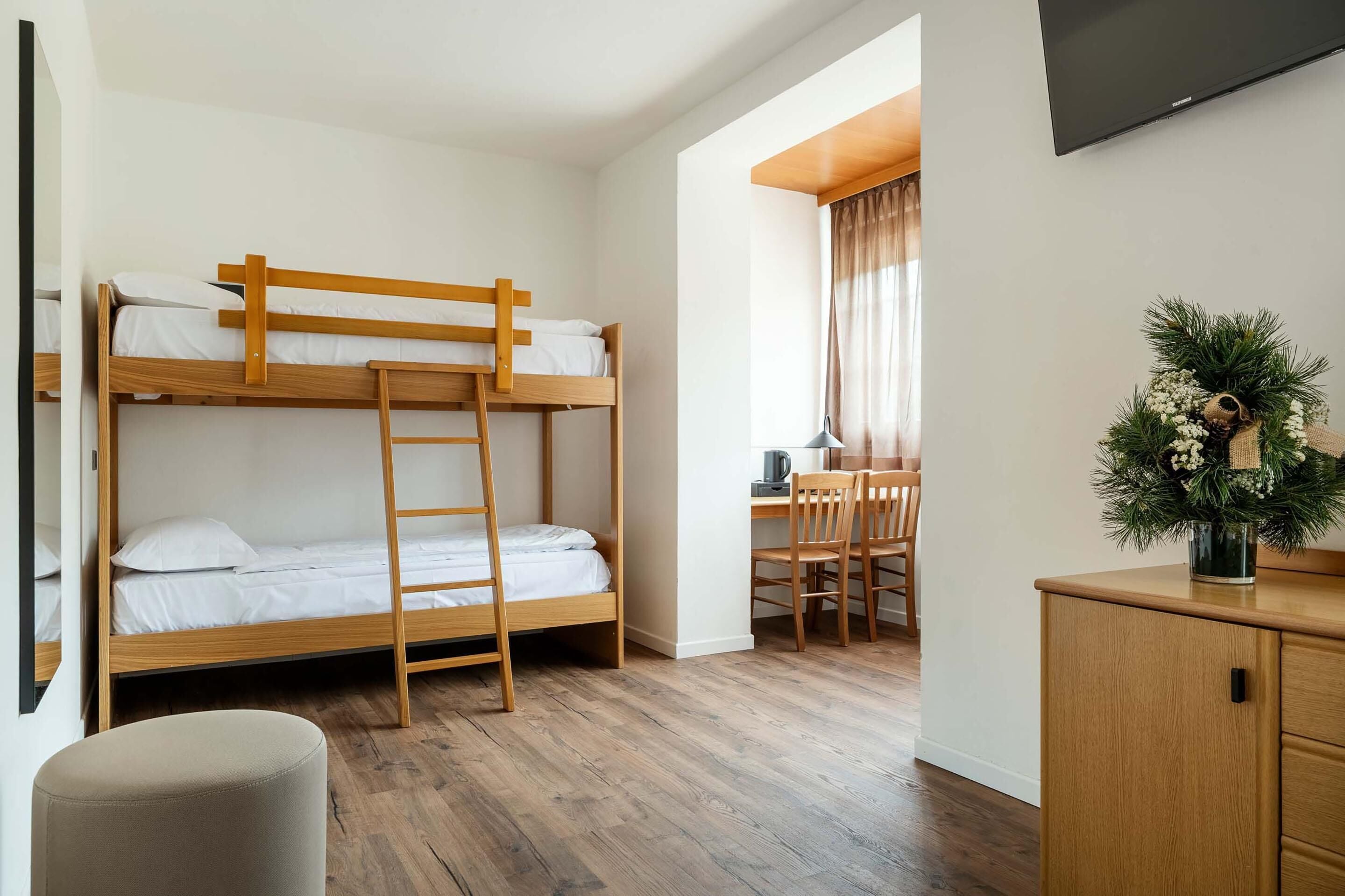 A bunk bed with a ladder, a desk with a chair, a television, and a cabinet.