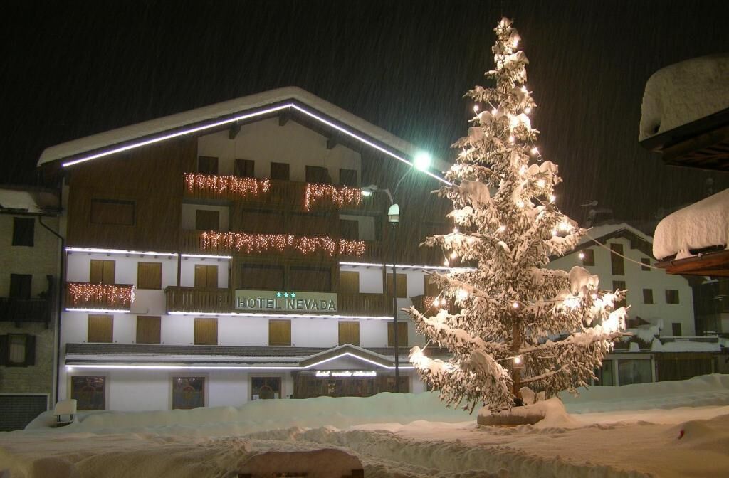 Un hotel con un árbol cubierto de nieve en primer plano, luces iluminadas y un letrero que dice "HOTEL NEVADA".