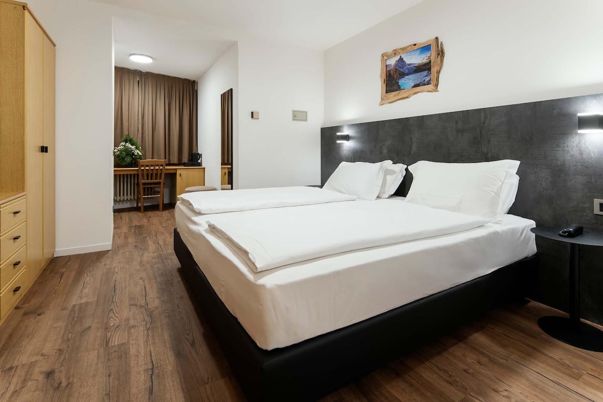 Ein Hotelzimmer mit Doppelbett, Schreibtisch mit Stuhl und einem kleinen Tisch mit Lampe.