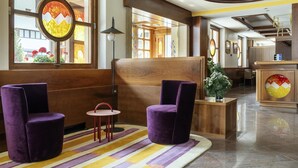 A lobby with purple chairs, a reception desk, and large windows with decorative glass panels. - Best Western Hotel Nevada (San Vito di Cadore)