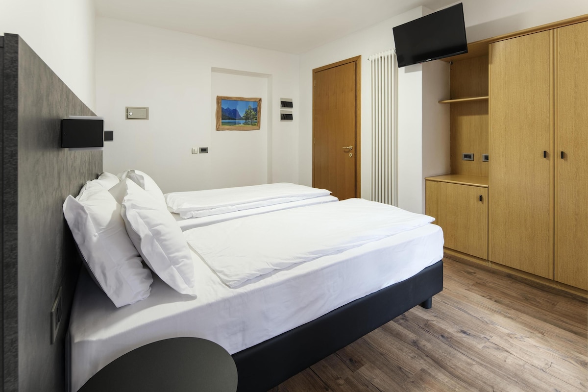 A bedroom with a bed, a wardrobe, a television, and a painting on the wall.