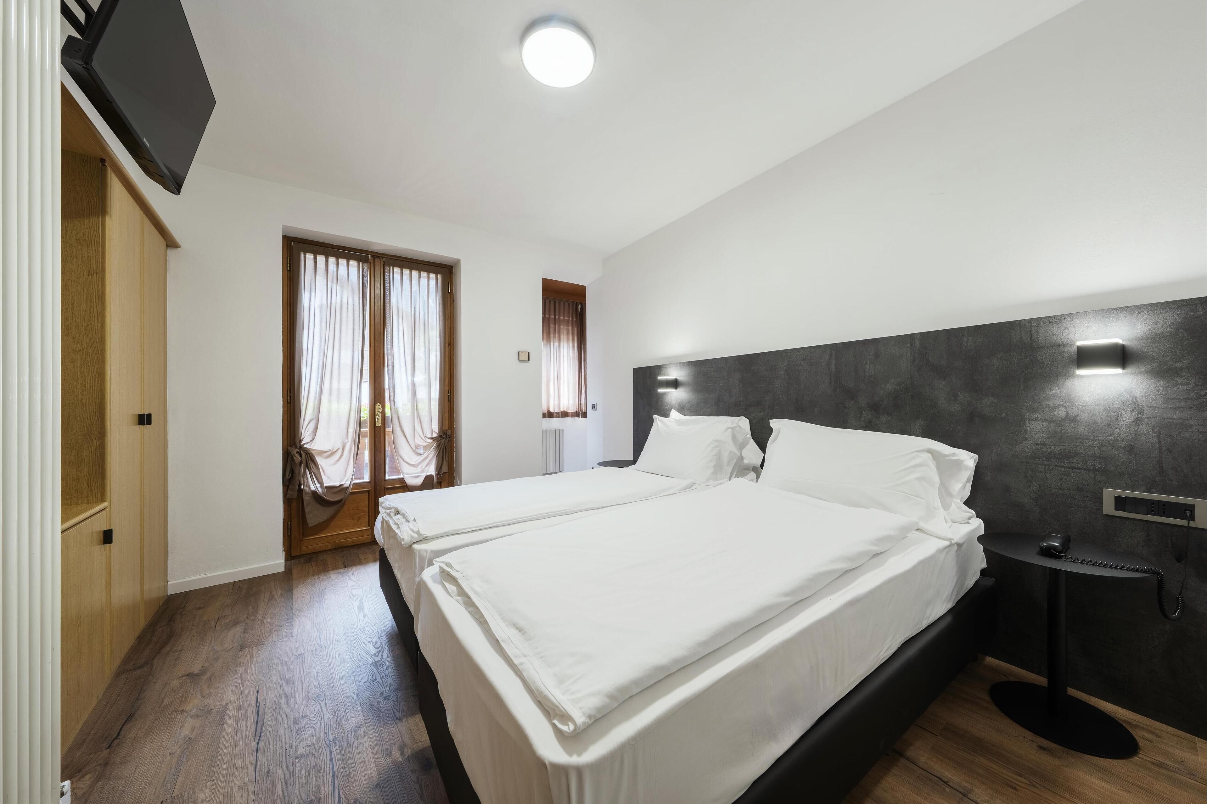 Una habitación de hotel moderna con dos camas, un televisor de pantalla plana, una mesita de noche con teléfono y una ventana con cortinas.