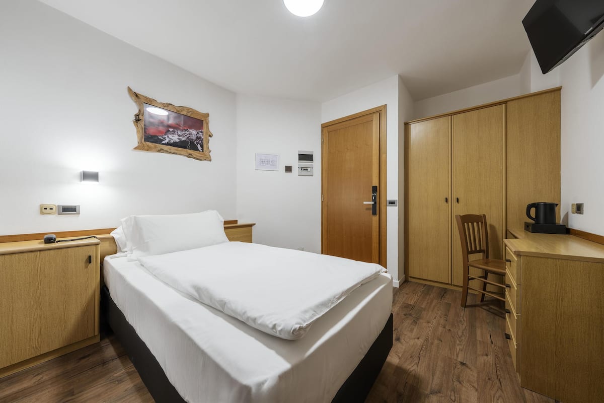 Ein Hotelzimmer mit Bett, Holzschrank, Schreibtisch, Stuhl und Fernseher.