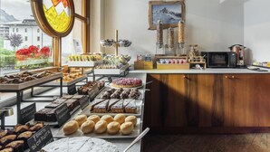 A bakery counter with various pastries and baked goods, a coffee machine, and a view of a mountain through a window. - Best Western Hotel Nevada (San Vito di Cadore)