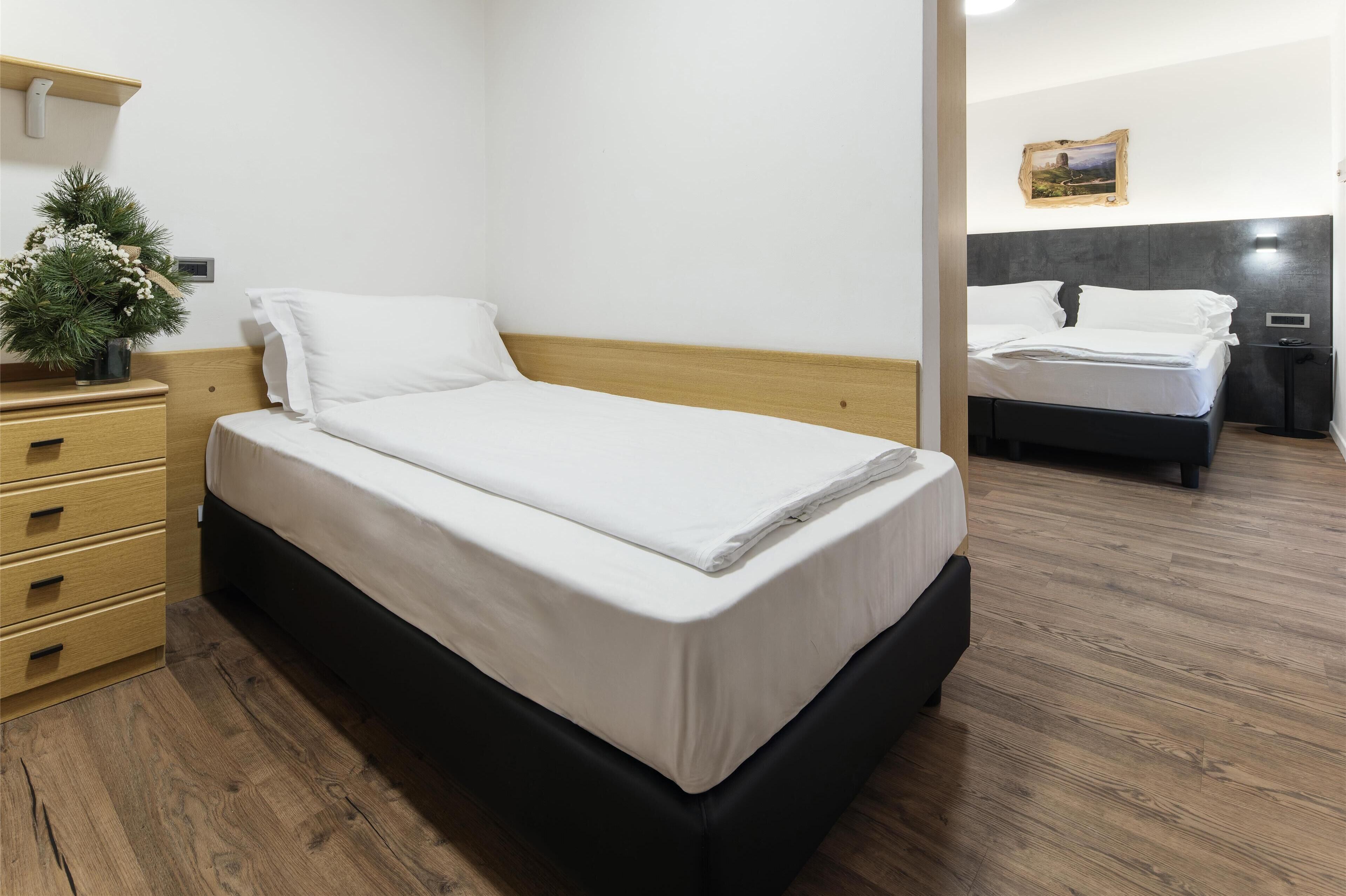 Una camera d'albergo con un letto singolo, una cassettiera in legno e una piccola pianta.