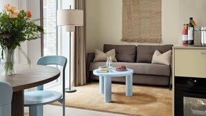 Un salon moderne comprenant un canapé, une table basse ronde, une table à manger avec des chaises, une lampe et un coin cuisine équipé d’appareils électroménagers.