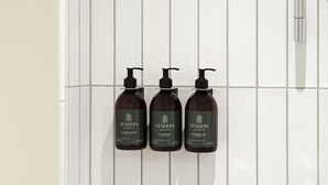 Trois produits de la marque Venders Copenhagen : après-shampoing, shampoing et gel douche, présentés sur un mur carrelé.