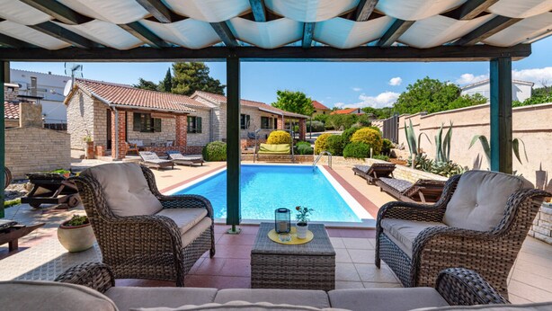 Uma área externa coberta com móveis de vime, piscina e vista para as casas vizinhas.