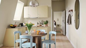 A modern kitchen with white cabinets, a dining table with four chairs, and a hanging light fixture. - Two-Bedroom Attic Apartment for 4 (København)