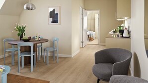 A modern living room with a dining area, a grey armchair, and a kitchen visible through an open door. - Attic Two-Bedroom Apartment for 6 (København)
