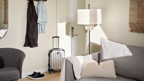 A hotel room with a grey sofa, a small armchair, a suitcase, a lamp, and a coat rack with hanging clothes. - Attic Two-Bedroom Apartment for 6 (København)