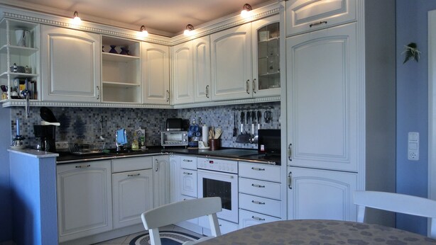 A kitchen with white cabinets, a built-in oven, and a dining table with a placemat. - Apartment for 2 pers. close to the beach approx. 700 m, incl. WLAN (Graal-Müritz)