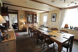 A dining area with a long wooden table, several chairs, a cabinet with dishes, and a window with curtains. - Upper Porthmawr - 5 Bedroom Cottage - Whitesands (Haverfordwest)