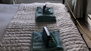 Ett sovrum med ett stort fönster, en säng med ett vadderat överkast och ett nattduksbord med en lampa och en liten växt.
