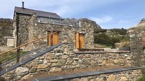A stone building with a wooden door and a staircase leading to a flat roof.