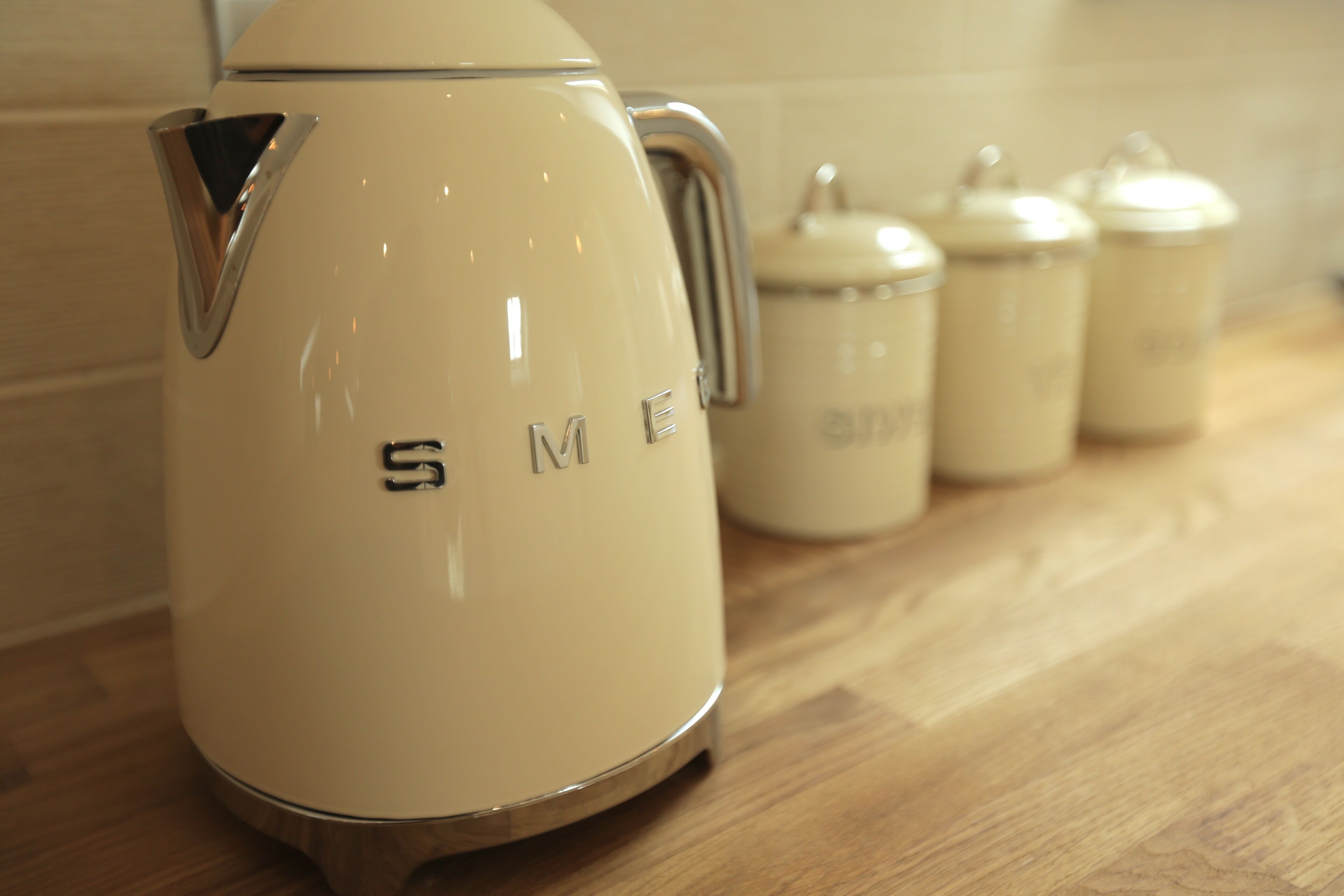 A cream-colored electric kettle with a handle on a wooden countertop.