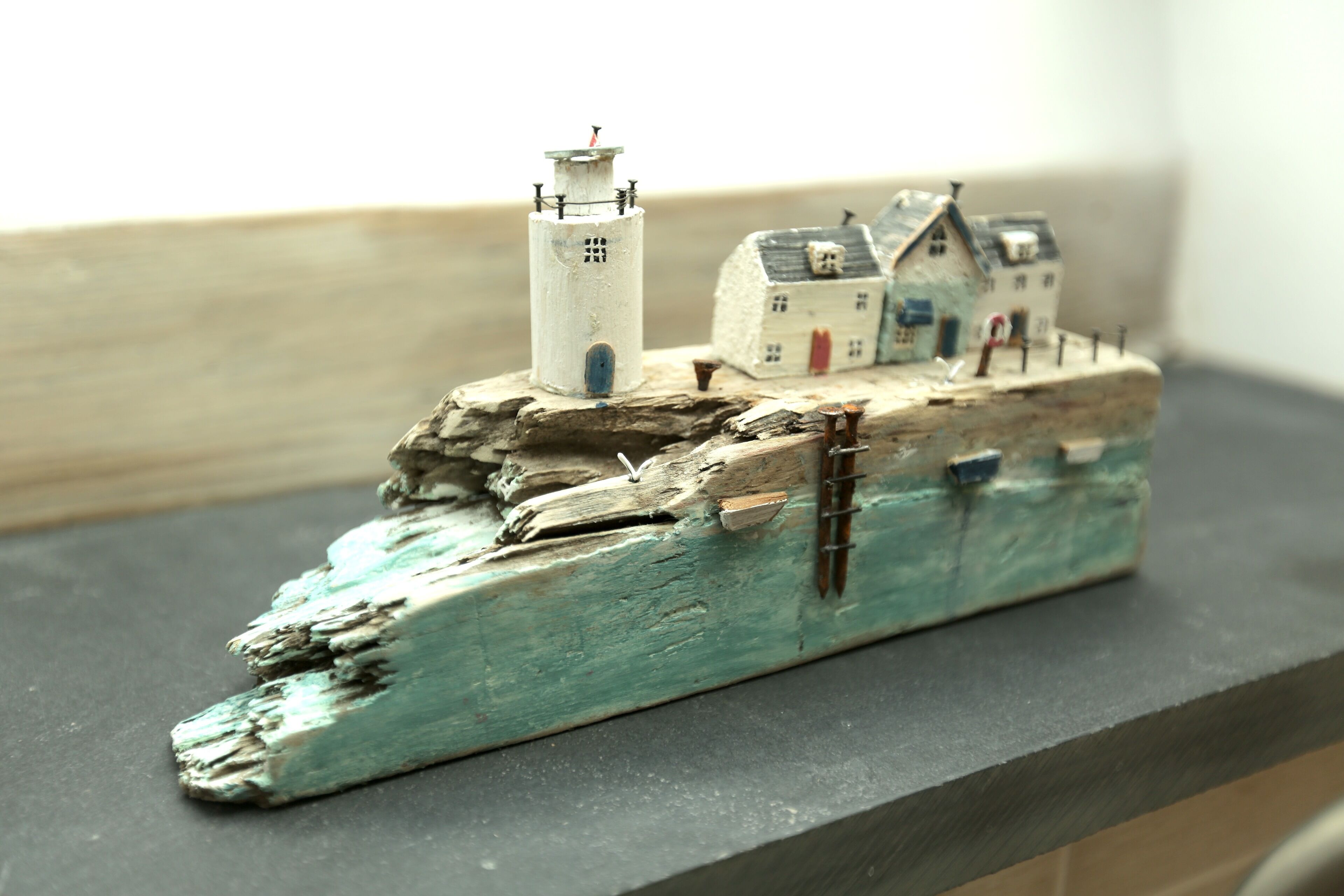 Un modelo de barco con un faro y dos casas sobre una base de madera.