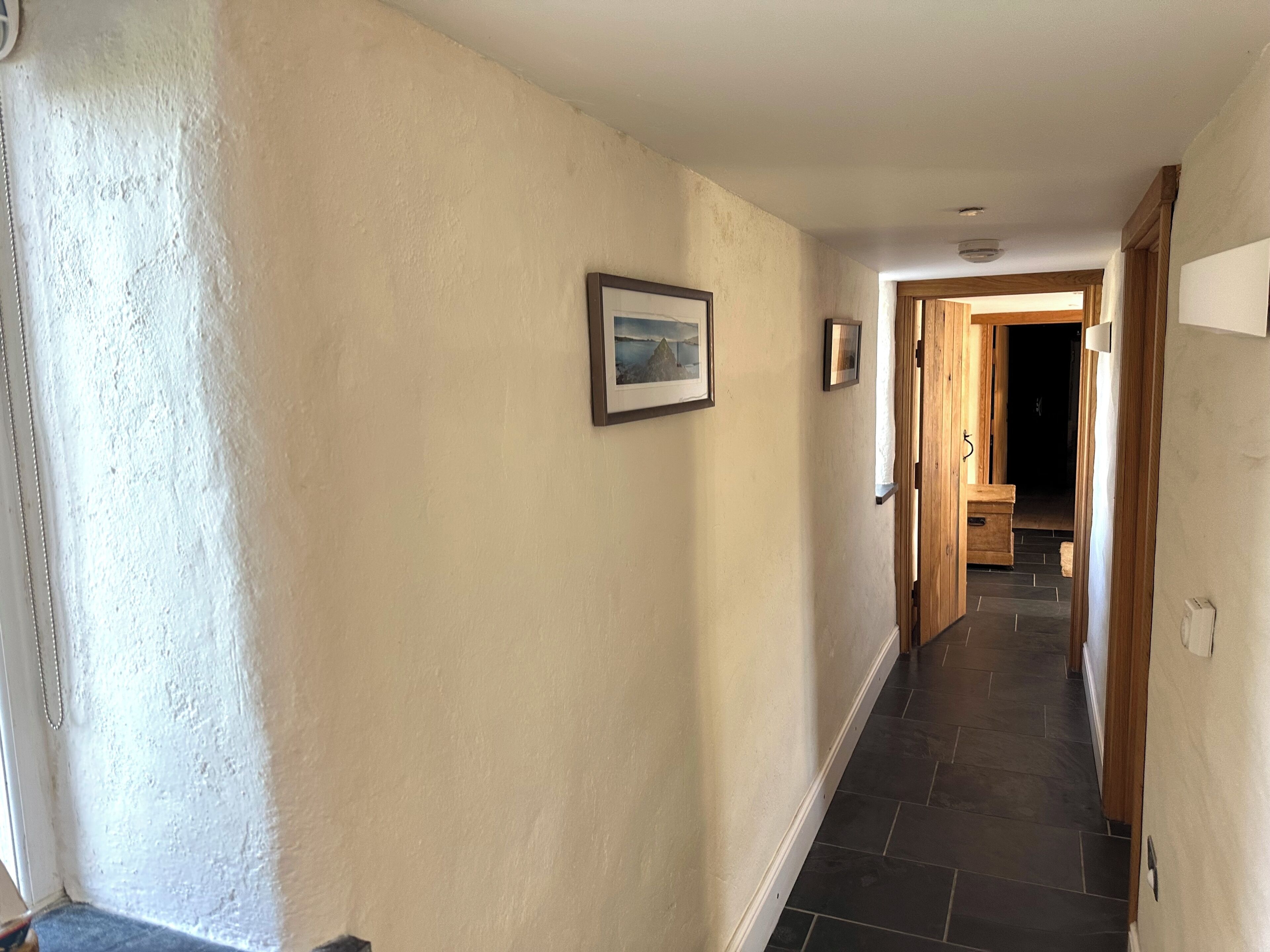 A hallway with a light-colored wall, a framed picture, and a door leading to another room.