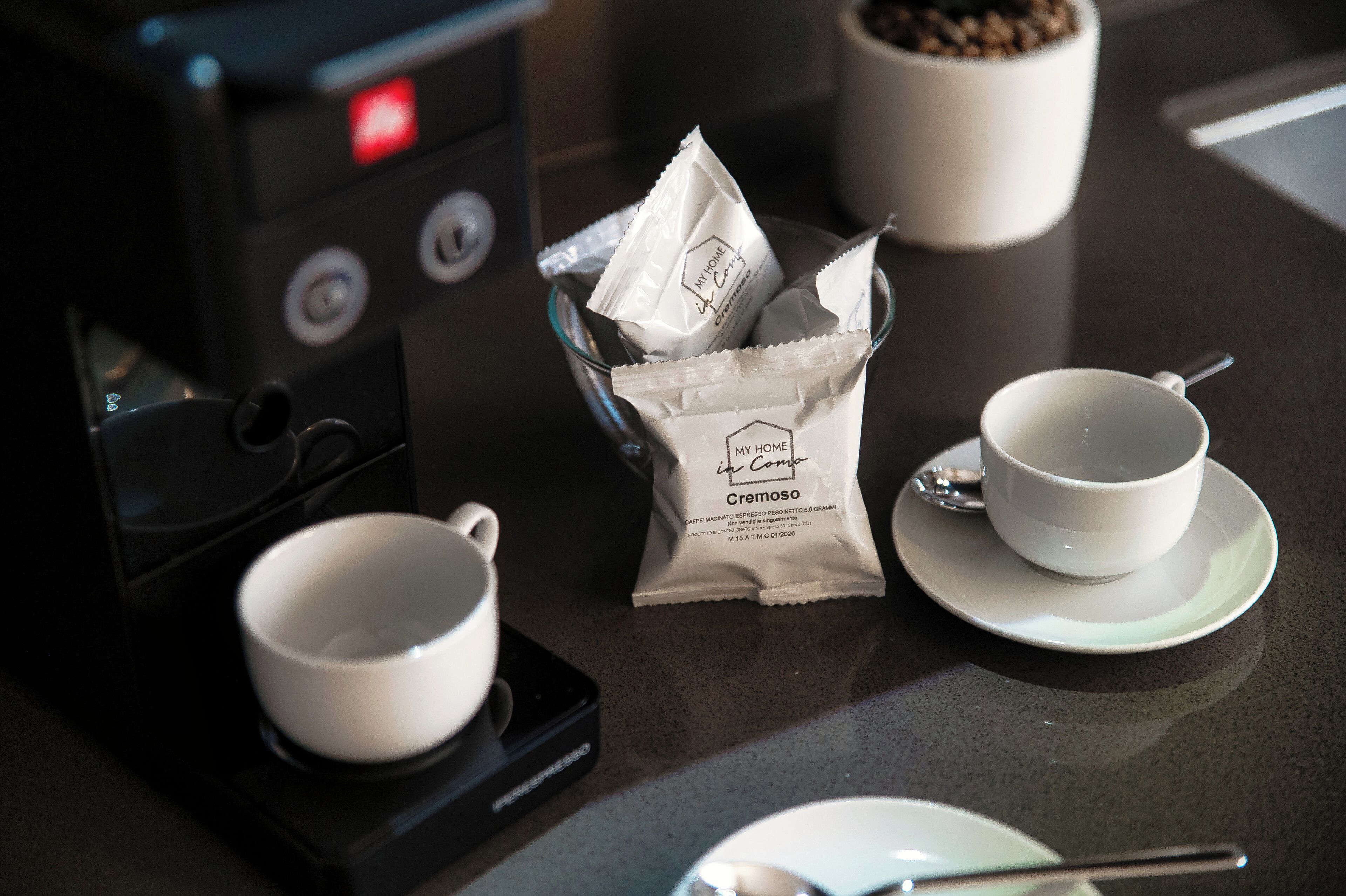 Uma máquina de café, duas chávenas, uma colher e um saco de café cremoso numa bancada.