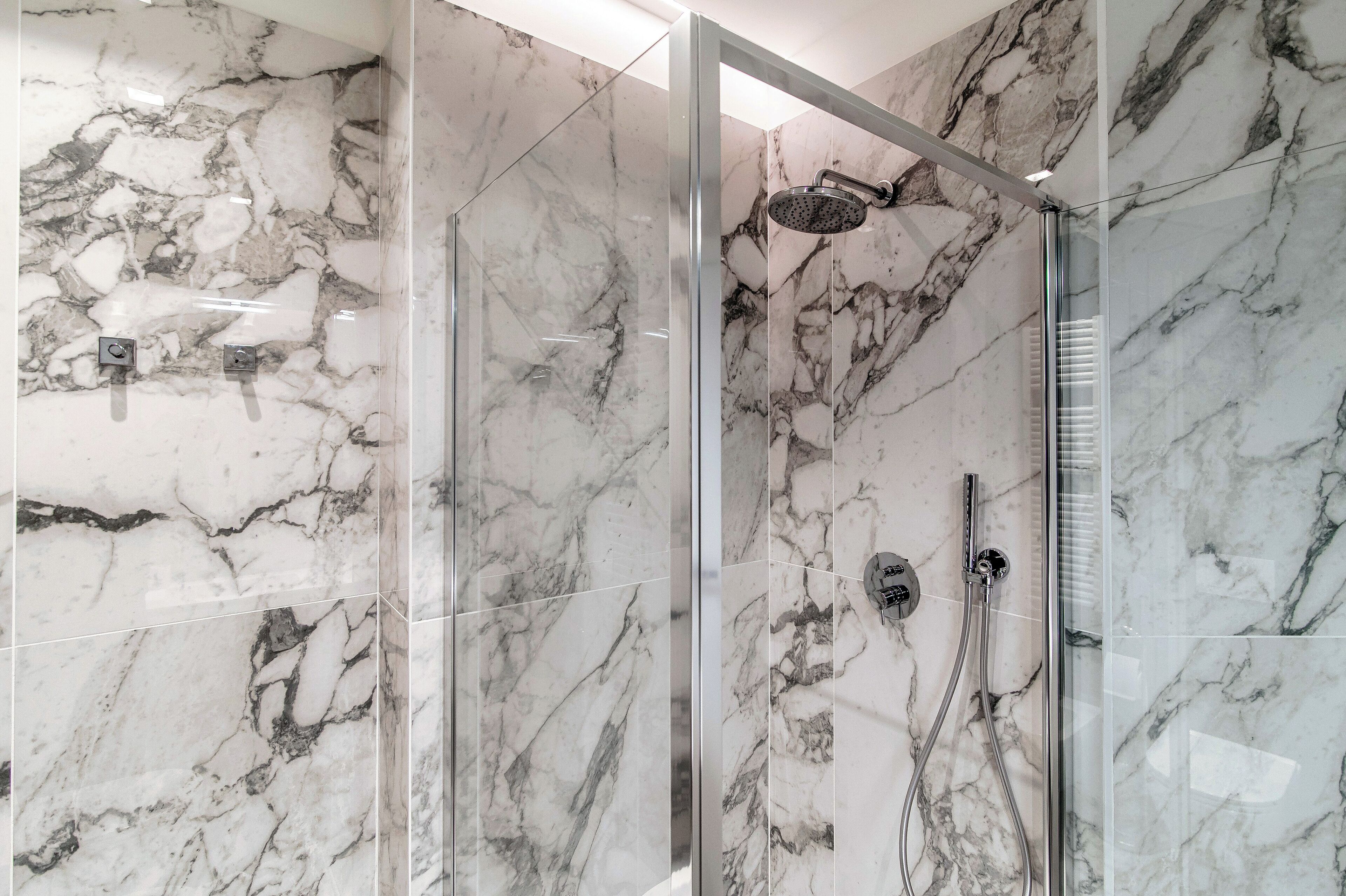 Un baño moderno con paredes de mármol y una zona de ducha con mampara de vidrio.