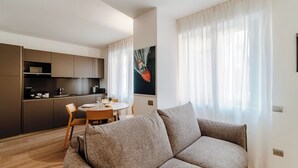 Uma sala de estar moderna com sofá, mesa de jantar com cadeiras, cozinha e uma janela grande com cortinas leves.