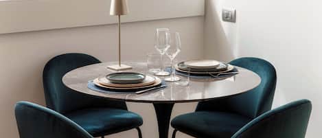 A round dining table with four dark blue chairs, set with plates, glasses, and a lamp.